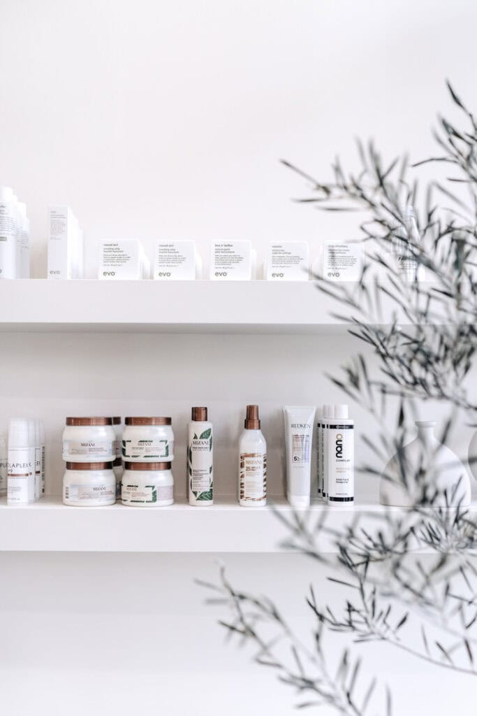 hairstyling products on a white shelf in a hair salon