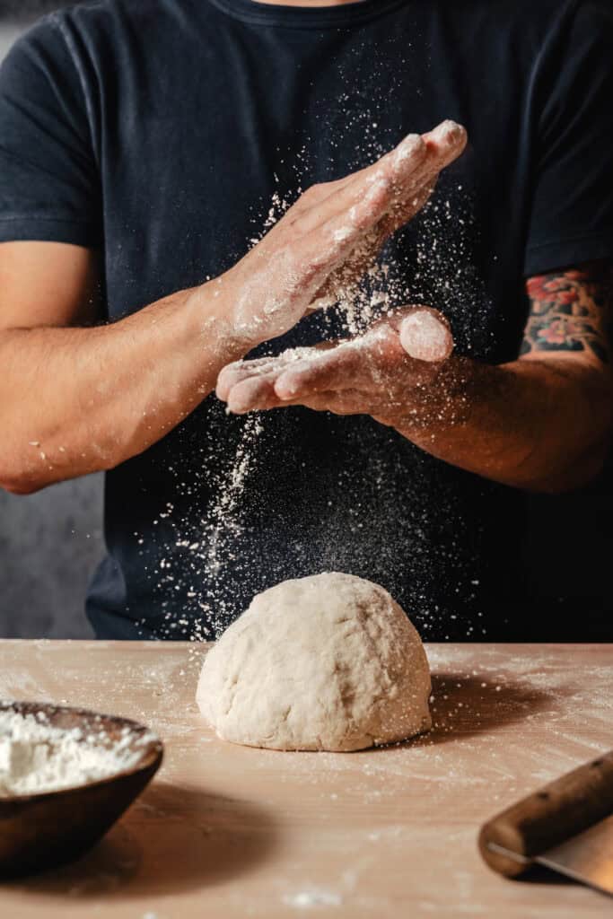 A chef knocks flour off of his hands after kneading pizza dough for a branding photography shoot